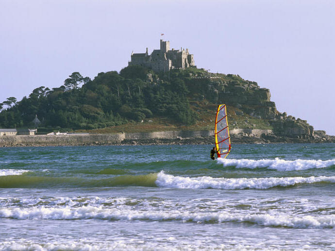 A person windsurfing off the coast of the castle on St Michael's Mount, Cornwall