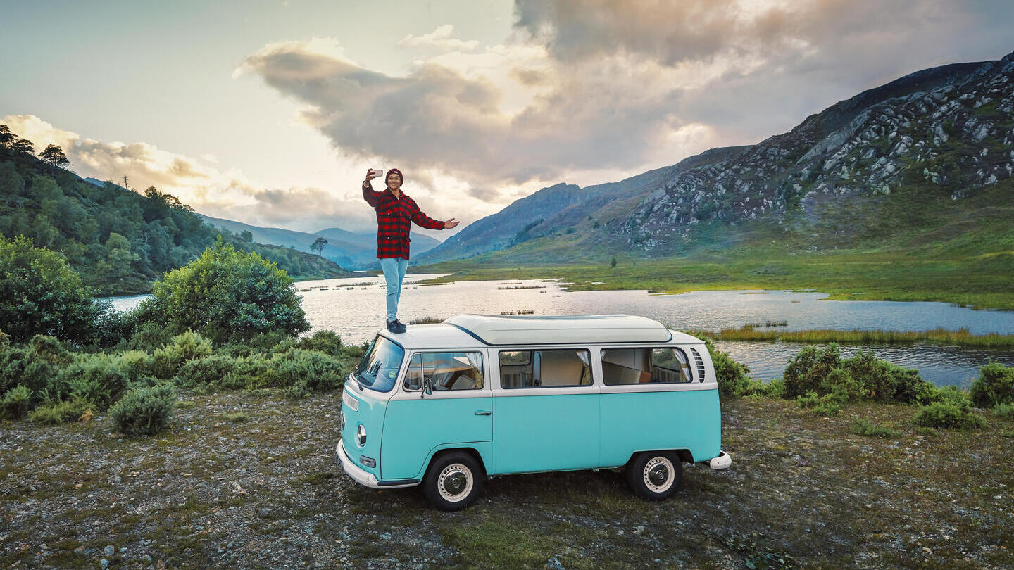 Man standing on camper van taking a selfie on the shore