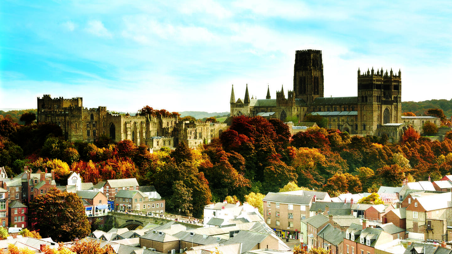 Historic stone buildings on a hill, including a large cathedral and castle, with colourful autumn trees and town below.