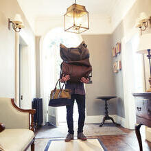 Man entering a beautiful hallway holding luggage covering his face and upper body