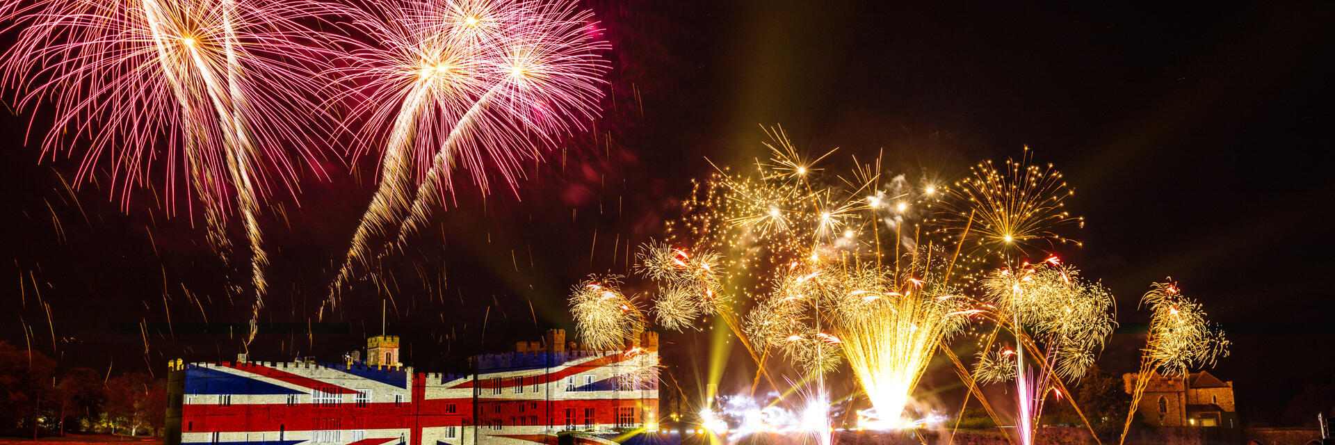 Fuegos artificiales y una gran iluminación con la bandera británica en la muralla de un castillo por la noche