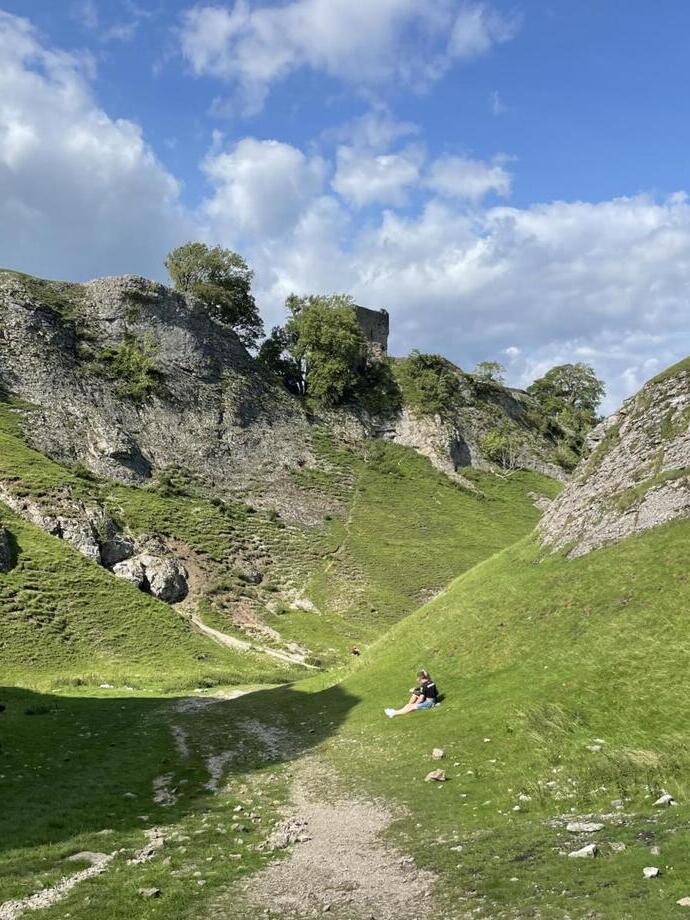 A valley on a bright summer's day, with a couple resting on the grass. A Castle is visible through the trees on the rocky hillside.