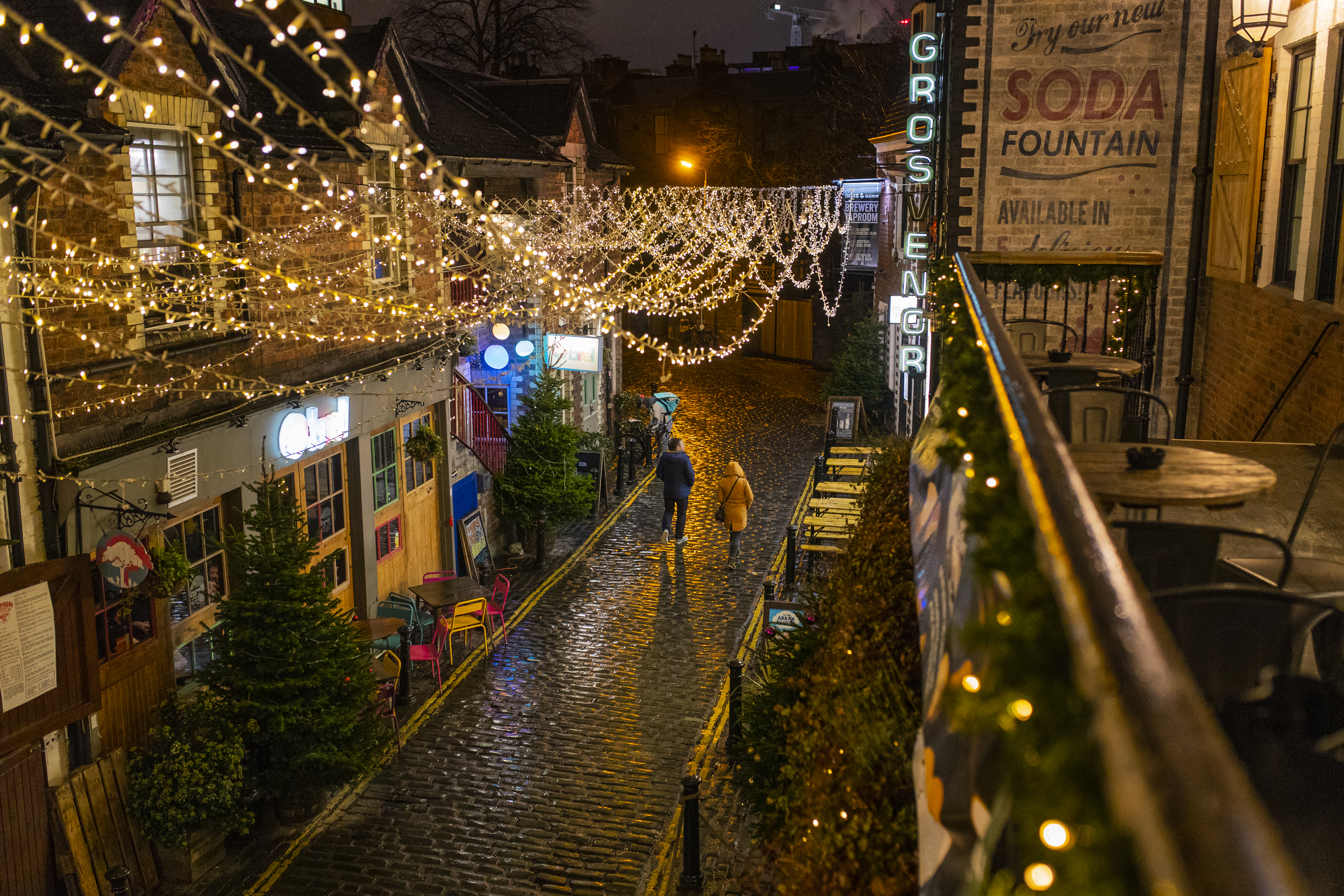 Couple marchant le long d'une rue pavée la nuit, décorée de guirlandes lumineuses