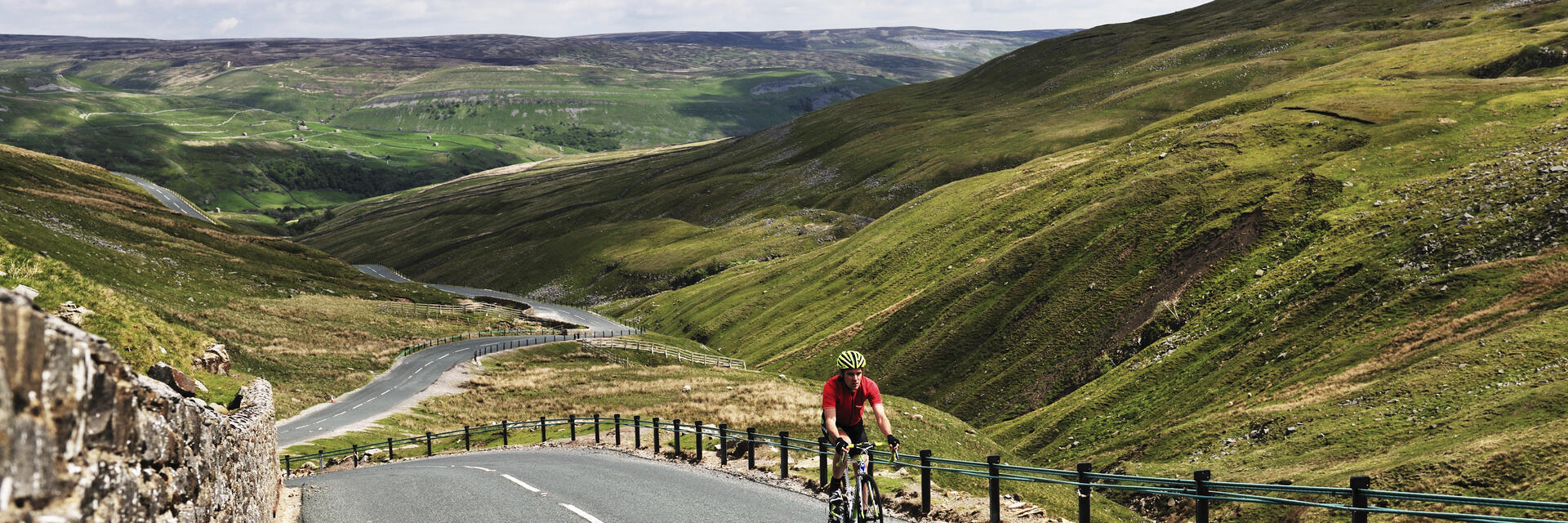 Cyclist riding on road through green dales