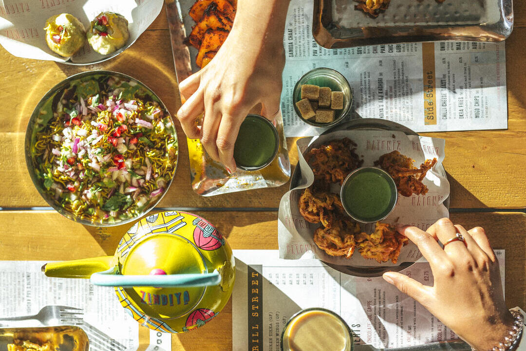 Menschen, die indisches Essen von einer Auswahl an Tellern auf einem Tisch essen