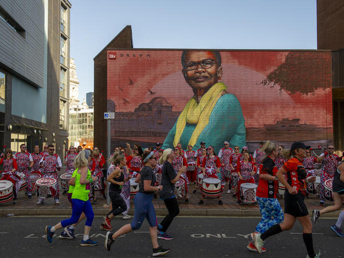 People running in front of a drumming band and colourful street art
