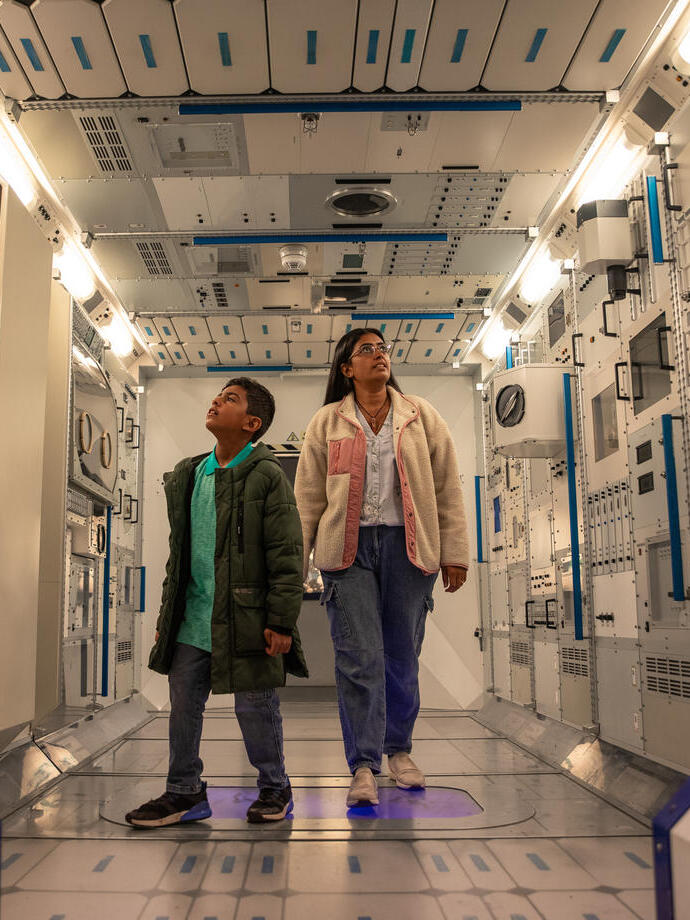 A woman and a boy walking through a replica space pod