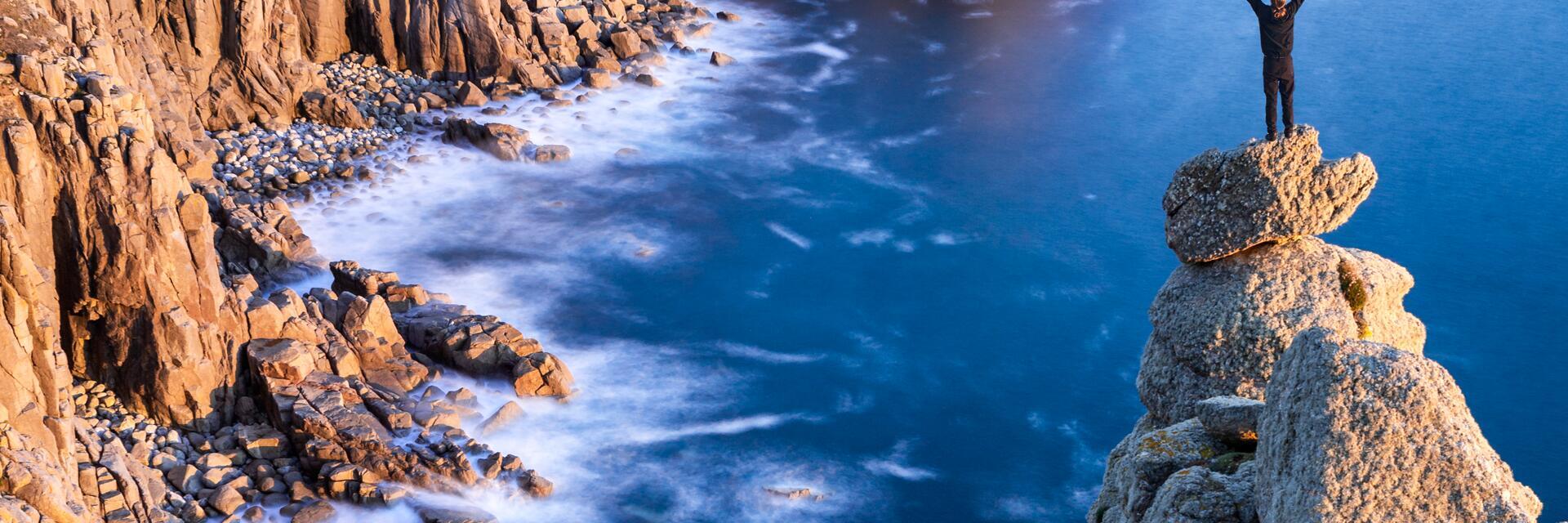 Mann, der auf einem felsigen Gipfel am Rande der Küste steht und über die Landzunge blickt