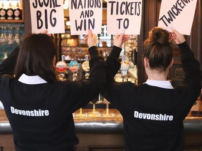 Due cameriere del Devonshire Balham Public House con cartelli che pubblicizzano biglietti gratuiti per il Sei Nazioni di rugby