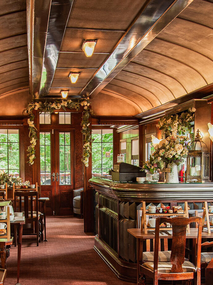 The inside of a wood panelled train carriage with tables and chairs on each side laid for afternoon tea. Bassenthwaite Lake Station - Silver award winner for New Tourism Business of the Year at the VisitEngland Awards for Excellence 2023.