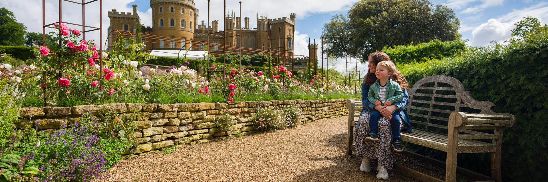 A woman sits on a bench with her child on her lap in front of a castle 