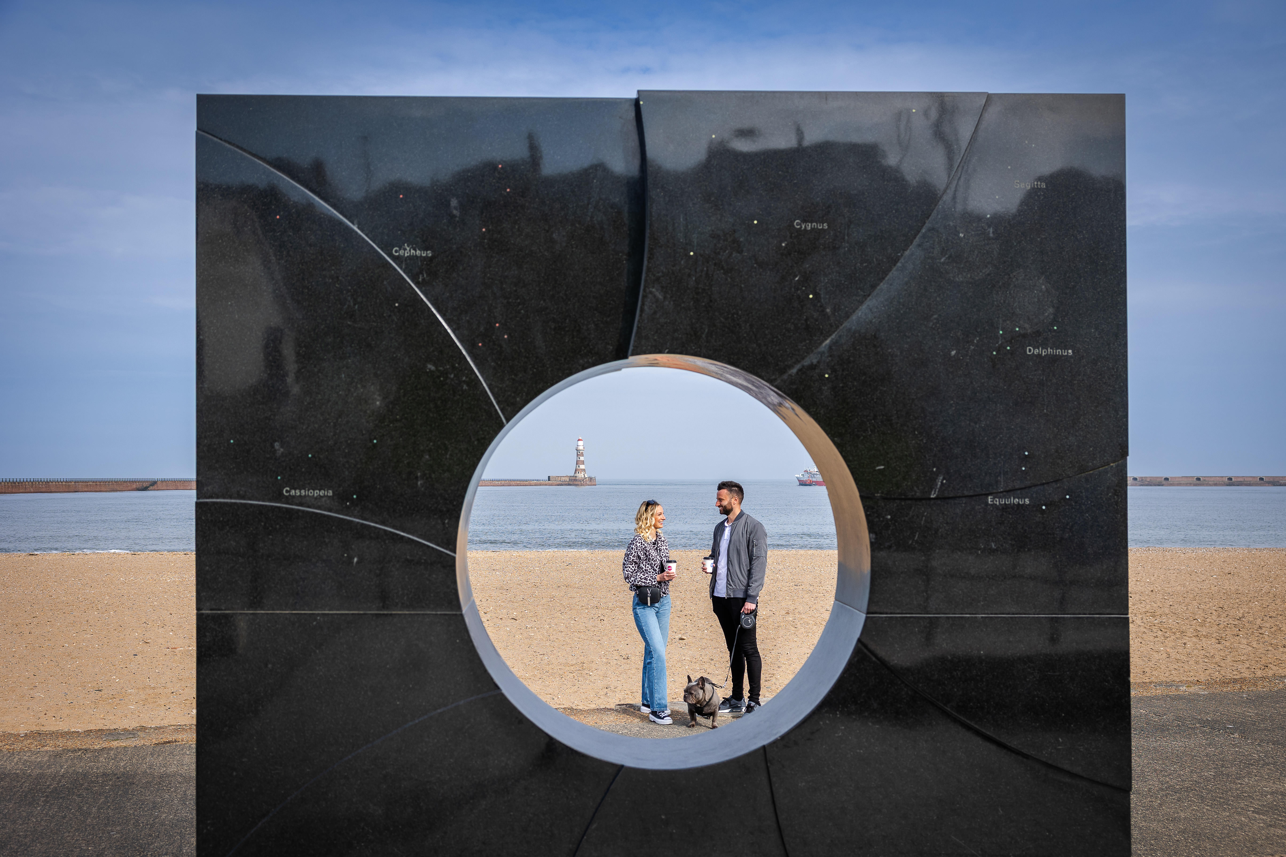 Two people seen through an art display on a beach sculpture trail.