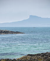 A man paddleboarding in the sea with a rocky outcrop in the distance.