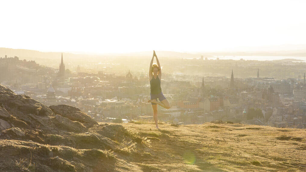Young woman doing yoga on a hill overlooking a city