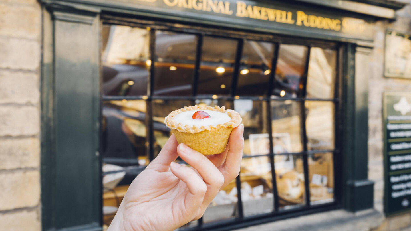 Hand holding Bakewell tart in front of bakery