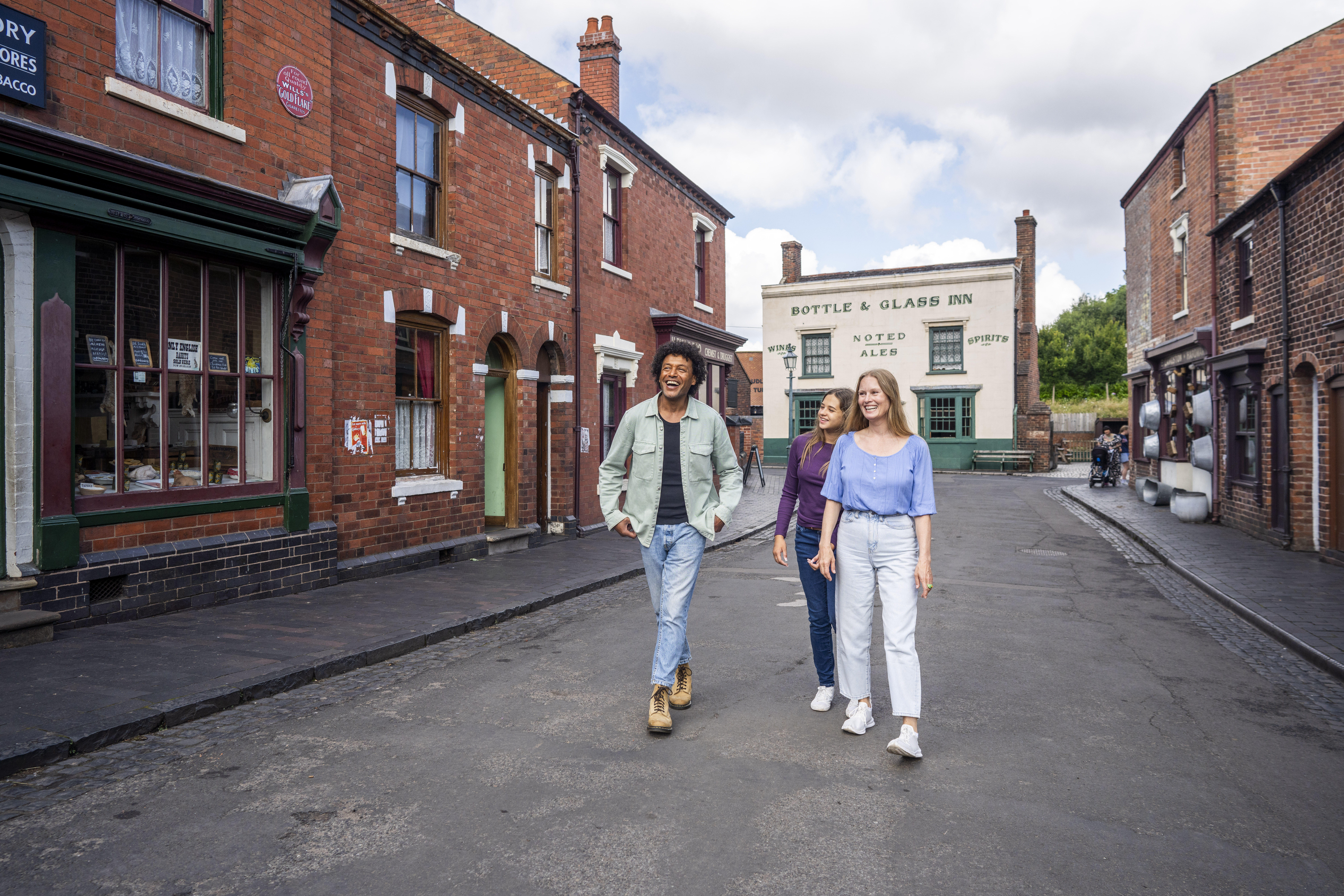 Three people walking and smiling in a historic-looking street with red brick buildings and a pub in the background.