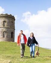 A young couple with a dog walking in Buxton Country Park with Solomon's Temple behind