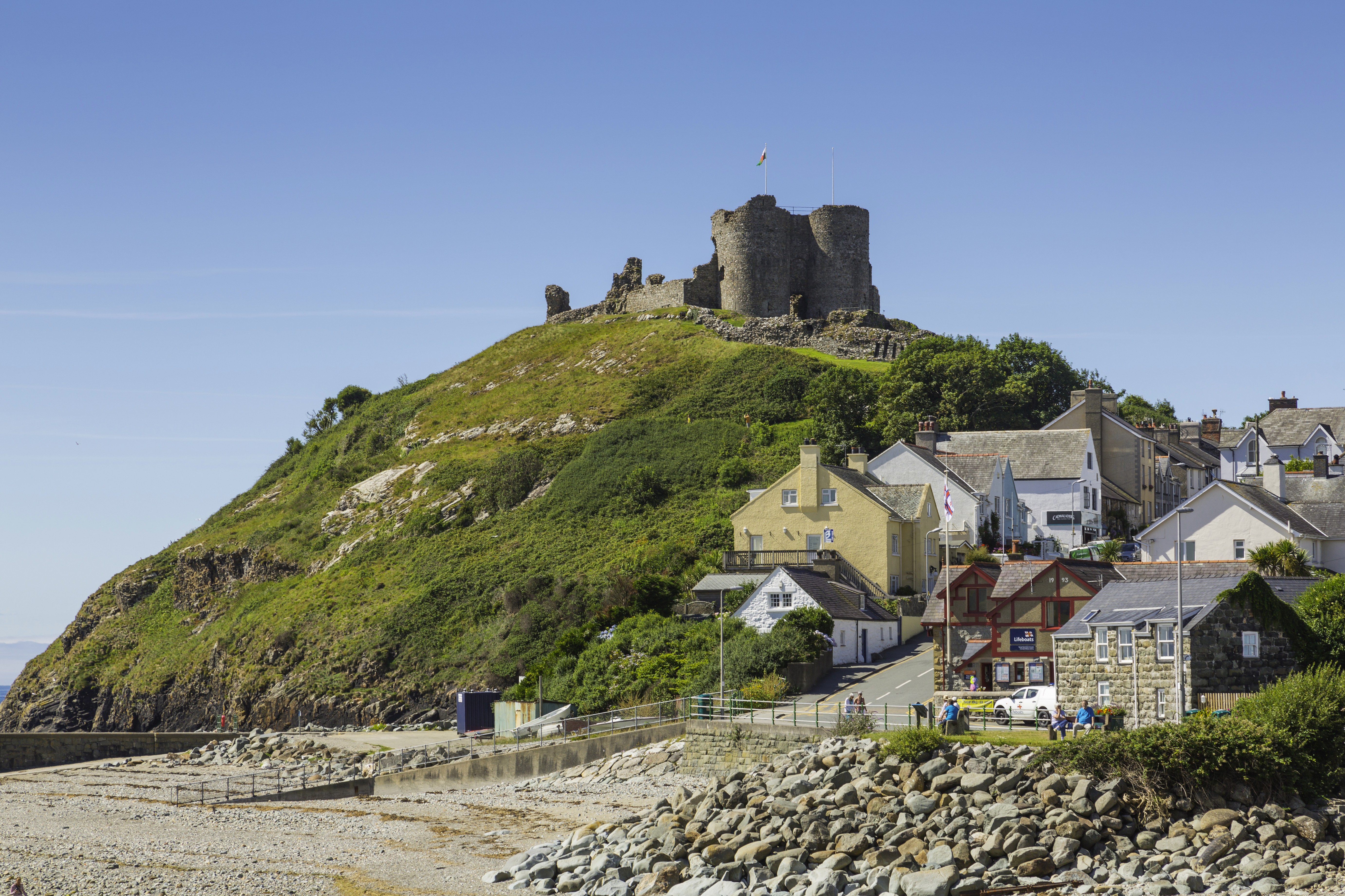 A castle on top of a hill beside a beach, surrounded by colourful buildings.
