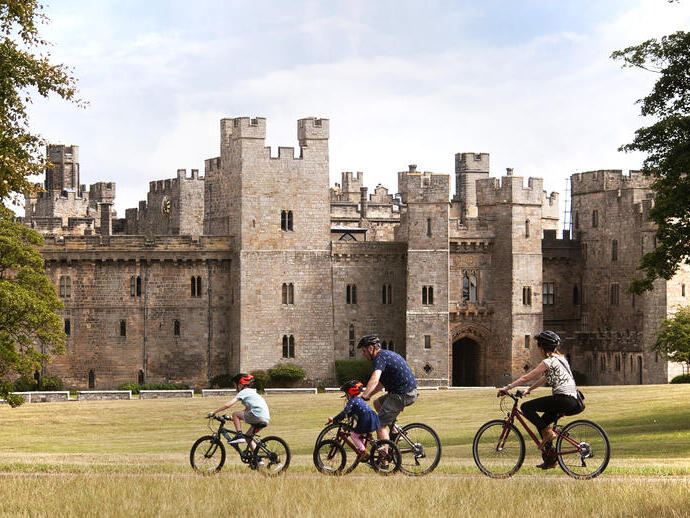 Familie, die mit dem Fahrrad an einer Burg im Nordosten Englands vorbeifährt