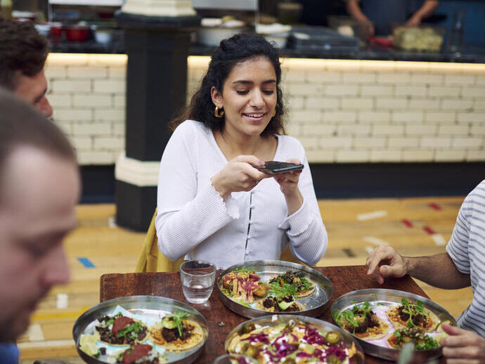 Femme assise avec des amis à une table, prenant une photo des plats dans une aire de restauration
