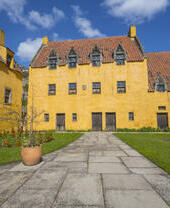 Un piccolo palazzo rustico dipinto di giallo con tegole rosse e un piccolo prato in una giornata di sole.