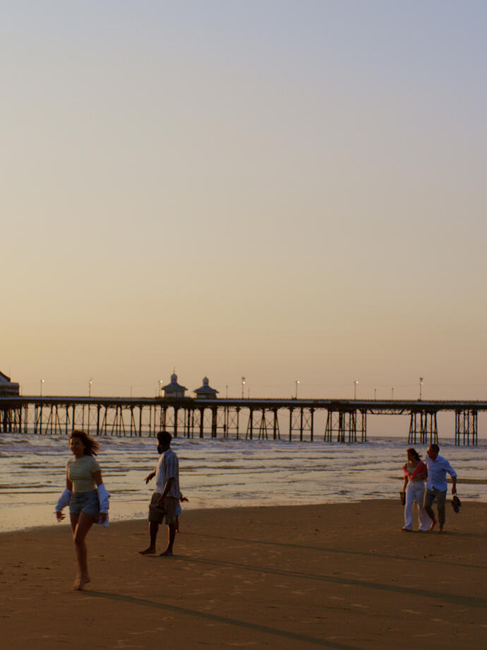 Groups of people enjoying the sandy beach with pier stretching out into the sea.