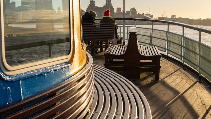 View from on board a ferry looking towards the city skyline with a Union Jack flag and two passengers on board