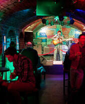 Man on stage playing a guitar in a club with arched ceilings