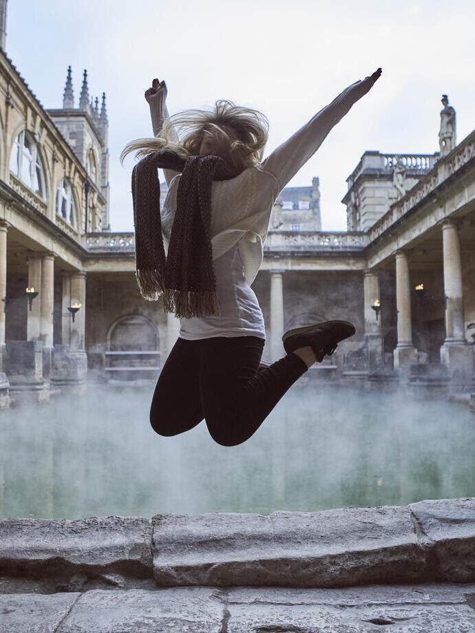 Woman leaping in the air at The Roman Baths, Bath, Somerset, England.