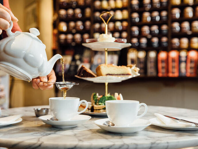 Person pouring cup of tea from white teapot in a tea shop