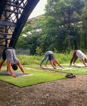 People practising yoga outside, beneath a bridge