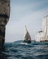 Person in canoe navigating coastline with cliffs in the background