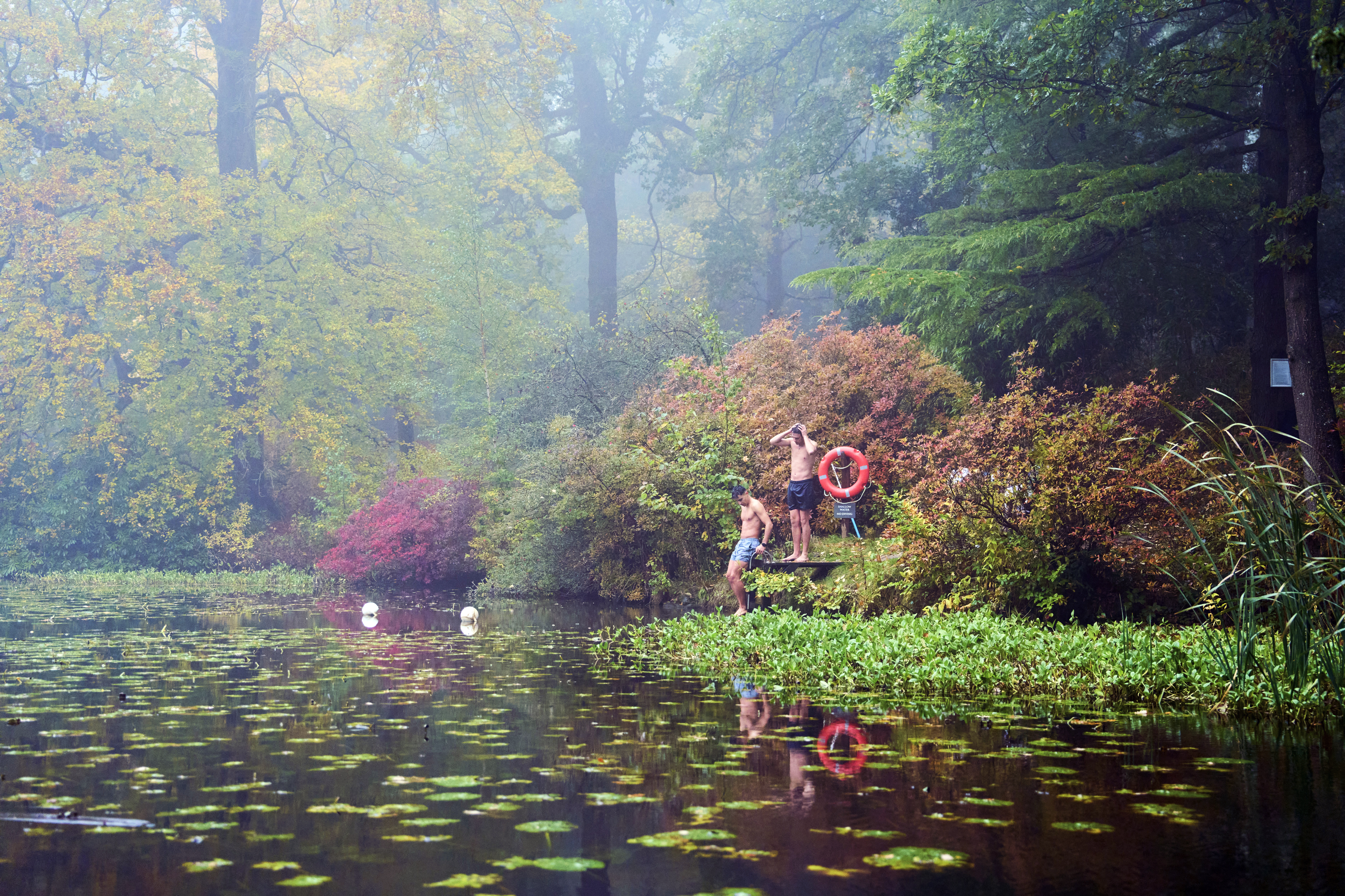 Twee mannen op het zwemplatform van een meer in een herfstachtige omgeving
