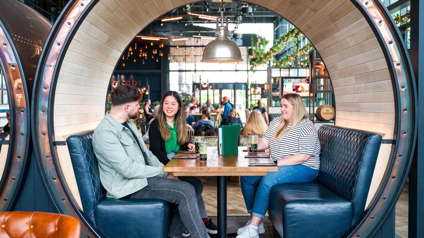 Two women and a man sit in a booth at a restaurant