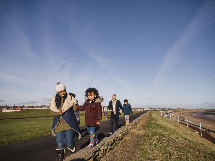 Family and friends walking along a coastal path in the winter sunshine