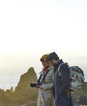 Couple standing on top of the cliffs, the woman holds a camera and the man wears a backpack