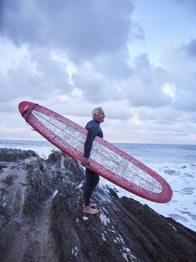 Man carrying surfboard and wearing wet suit on the rocks