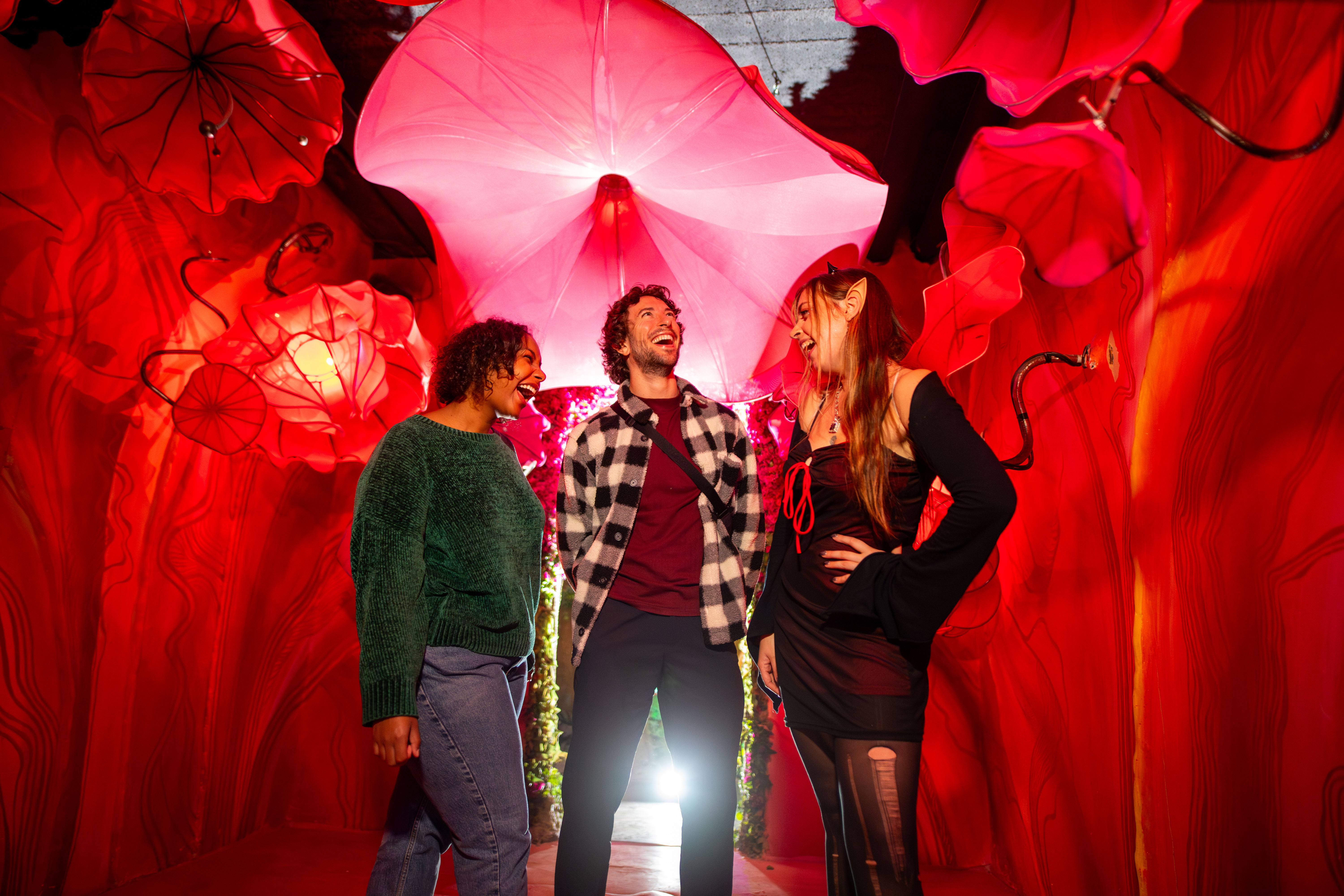 Three friends standing and laughing under a red illuminated canopy