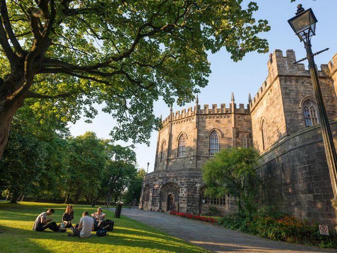 External view of Lancaster castle with visitors sitting around the lawn in the foreground