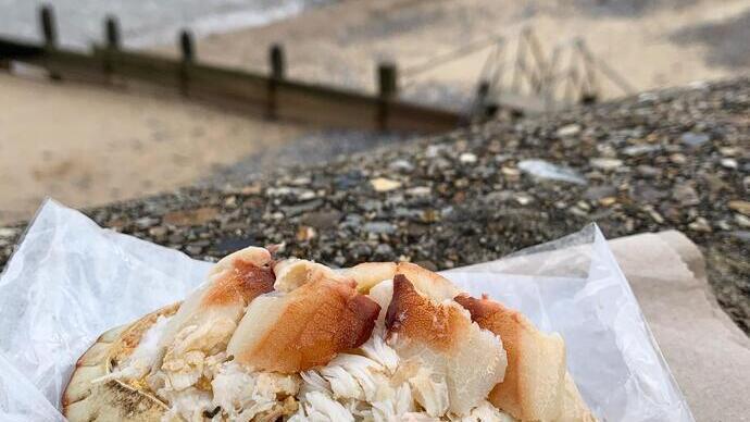 Ein Teller mit Krabben auf einer Serviette, im Hintergrund der Strand und das Meer
