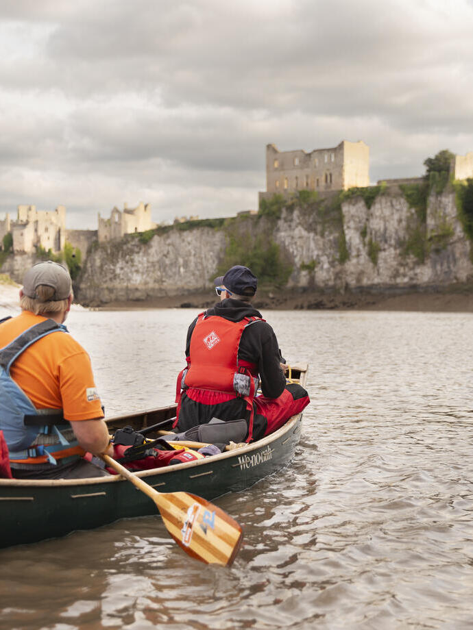 Due persone in canoa lungo un fiume con vista su un castello sullo sfondo.