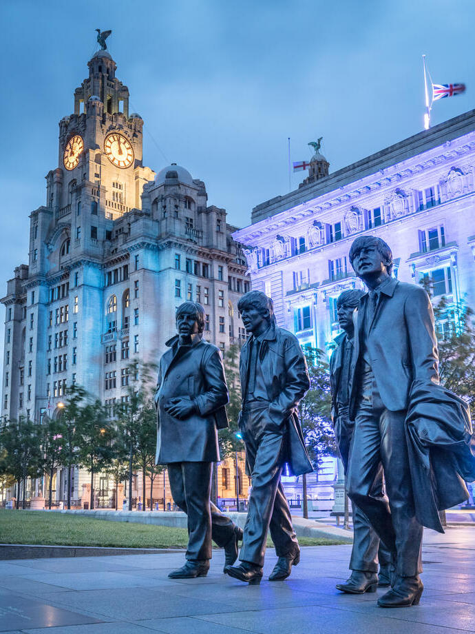 The Beatles sculpure and Three Graces buildings lit up in the evening.