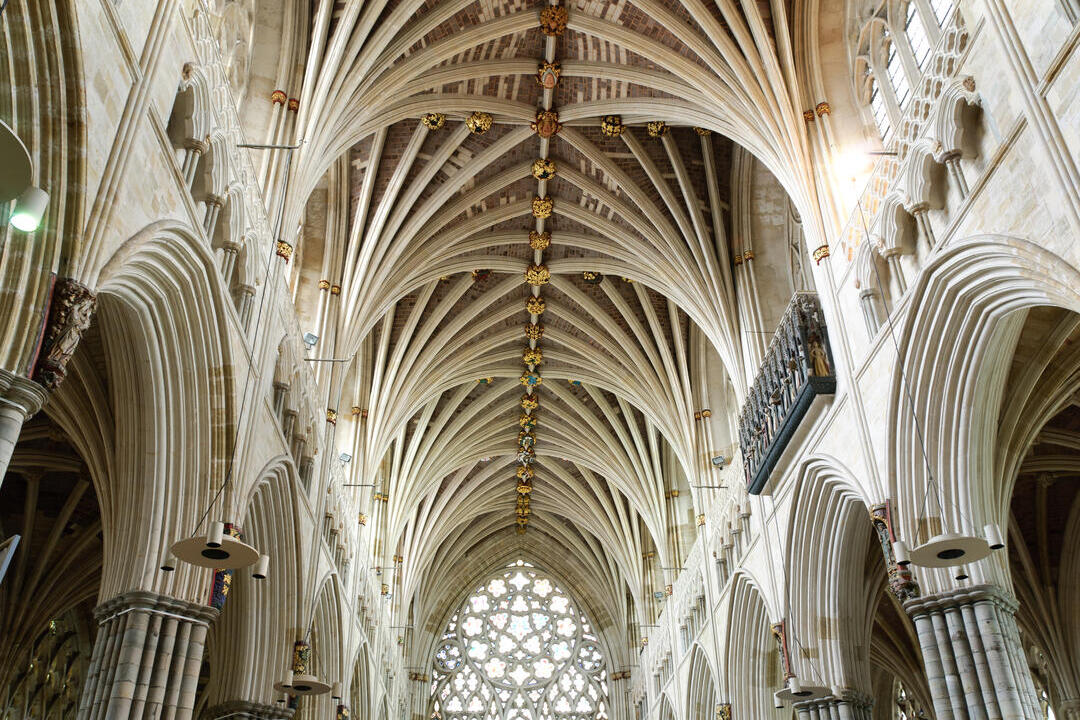 The vaulted ceiling of a Gothic cathedral with intricate stonework and decorative bosses, viewed from the nave.