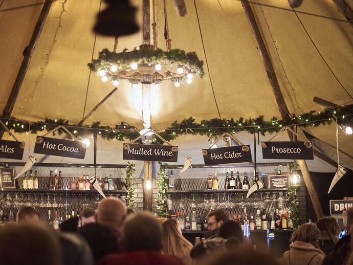 People in front of a bar in a marquee, lit with fairy lights