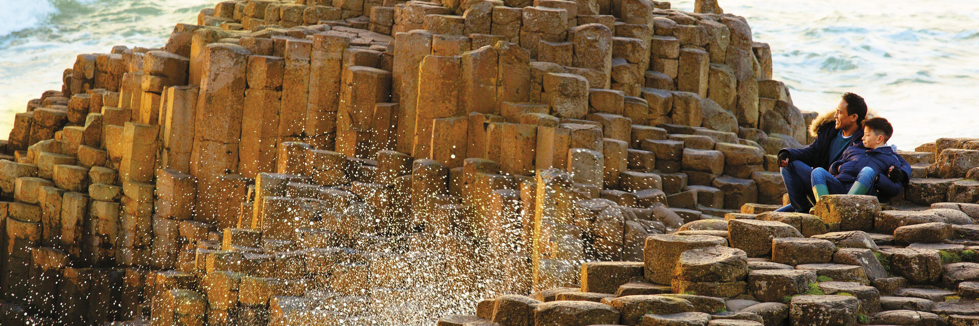 Man and child sitting on rock formations by the sea