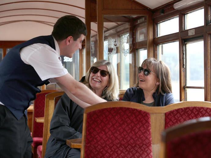 Pasajeros de un tren histórico hablando con un miembro de la tripulación.