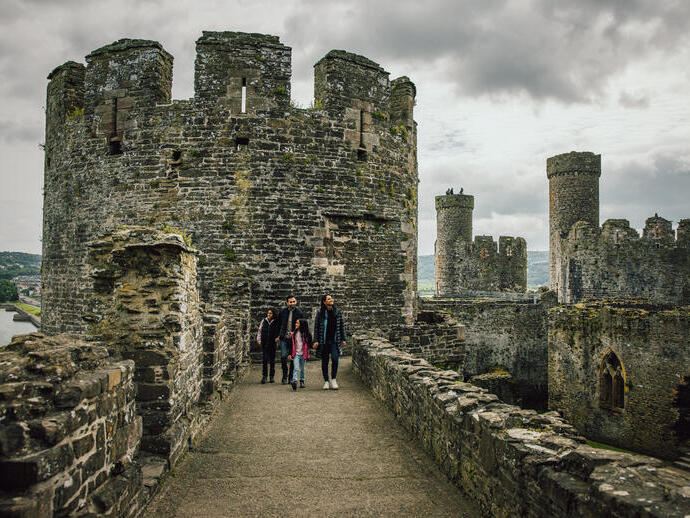 Una famiglia cammina su un muro di un antico castello di pietra sotto un cielo nuvoloso