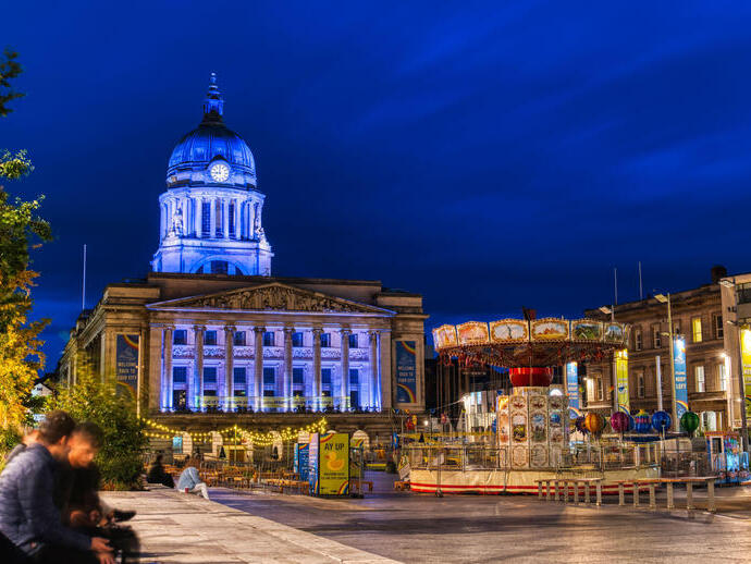 Evening view of city square with large municipal building and a merry go round.