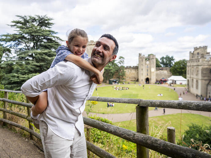 A man holds his daughter on his back in front of a heritage castle