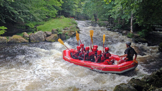 A group of children in a large dinghy with an instructor going down some what water rapids